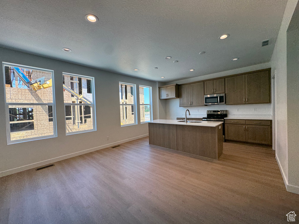 Kitchen with stainless steel appliances, light wood finished floors, a center island with sink, recessed lighting, and light countertops