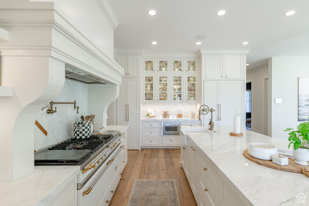 Kitchen featuring recessed lighting, light wood-style floors, decorative backsplash, white cabinets, and light stone counters