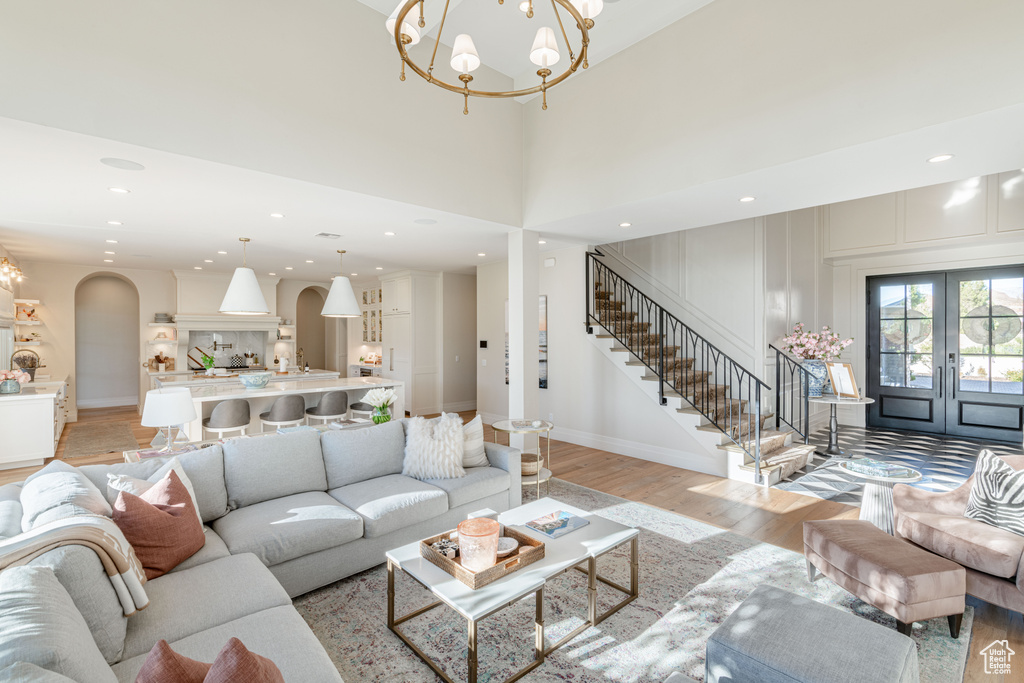 Living room featuring french doors, light wood-style flooring, a chandelier, stairway, and recessed lighting