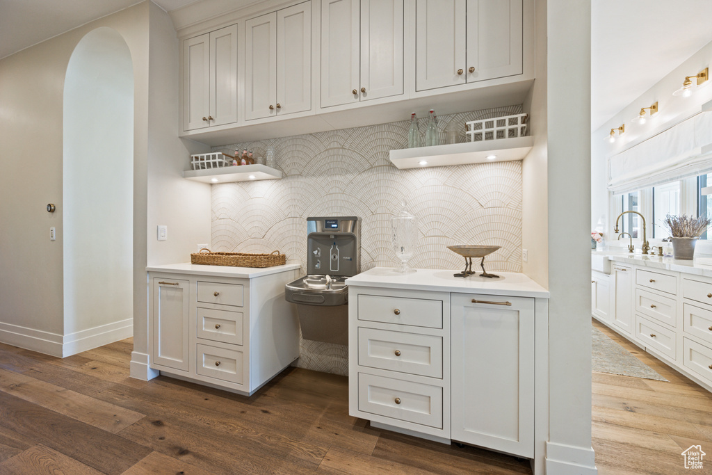 Kitchen featuring open shelves, tasteful backsplash, dark wood-type flooring, light countertops, and arched walkways