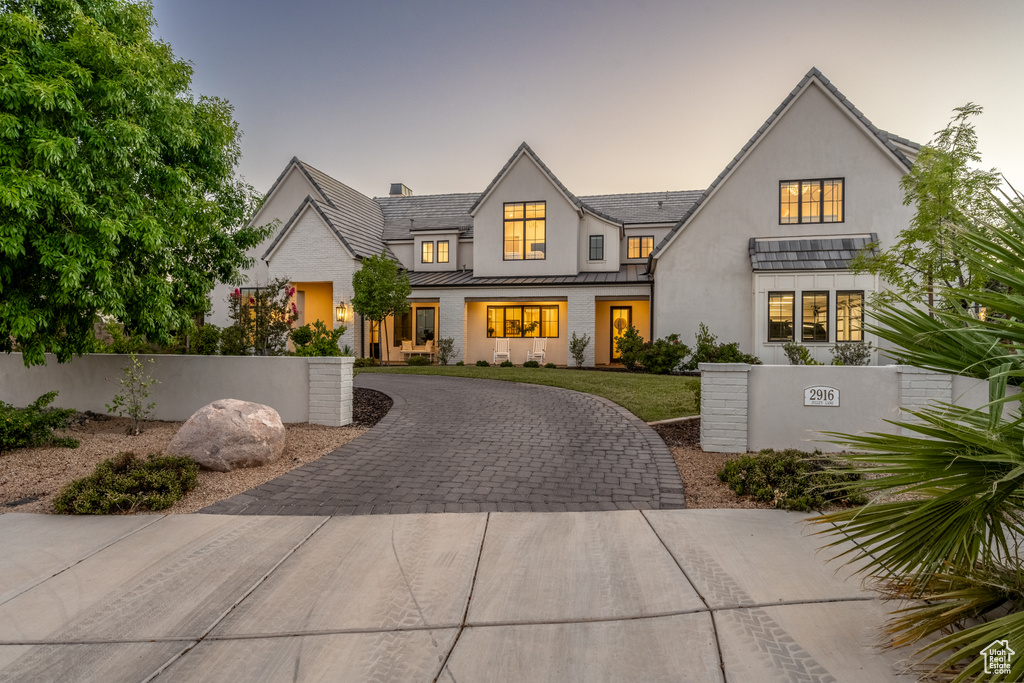 View of front of house with a standing seam roof, curved driveway, stucco siding, and a metal roof