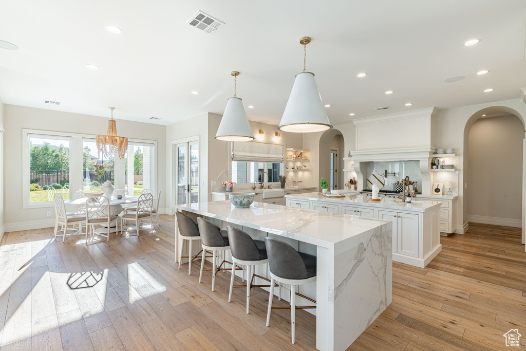 Kitchen featuring arched walkways, a spacious island, white cabinets, light wood-type flooring, and recessed lighting