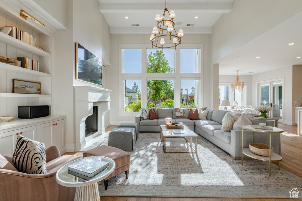 Living room with a chandelier, light wood-type flooring, built in features, a towering ceiling, and a high end fireplace