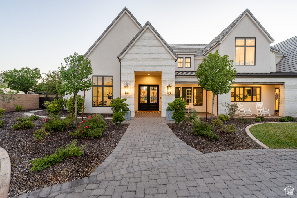 View of front facade featuring french doors, brick siding, stucco siding, and a standing seam roof
