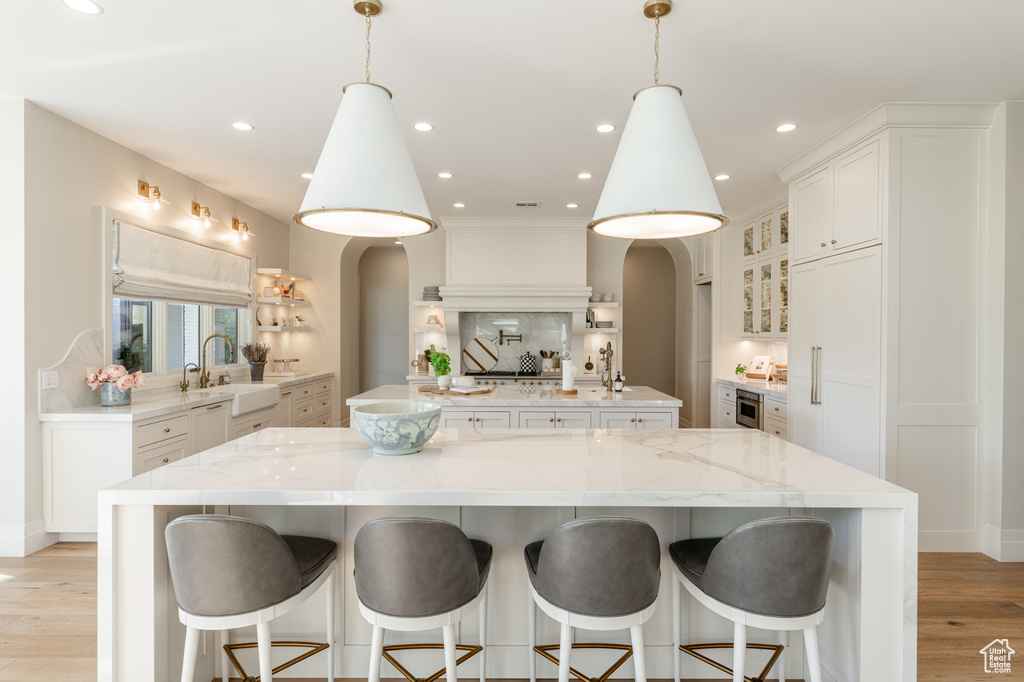 Kitchen featuring a spacious island, arched walkways, tasteful backsplash, light wood-type flooring, and white dishwasher