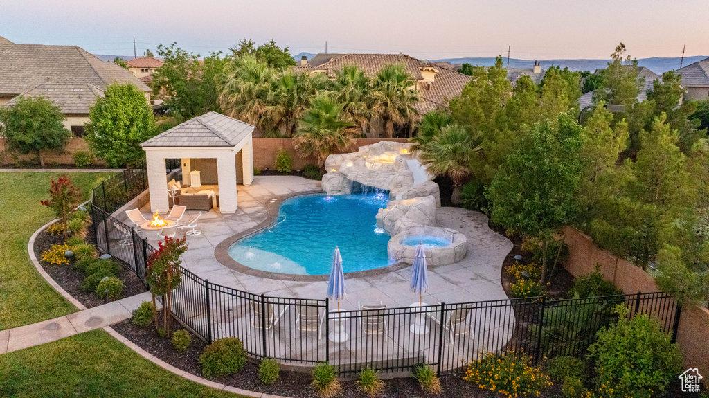 Pool at dusk with a patio, an outbuilding, a storage structure, a pool with connected hot tub, and an outdoor living space with a fire pit