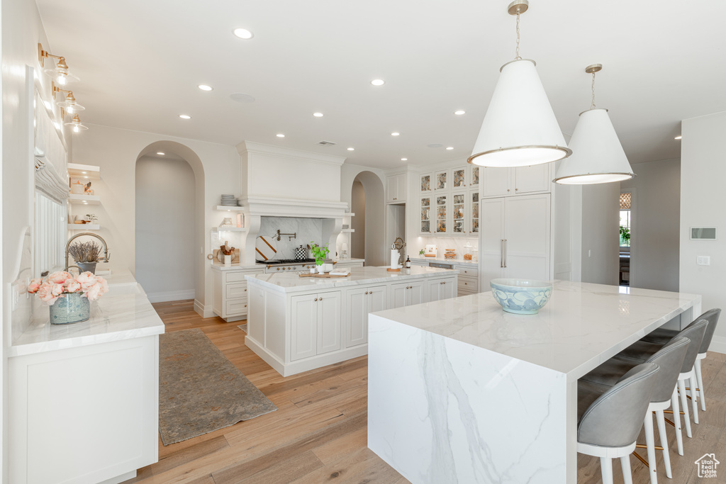 Kitchen with arched walkways, a large island, light wood finished floors, recessed lighting, and white cabinets