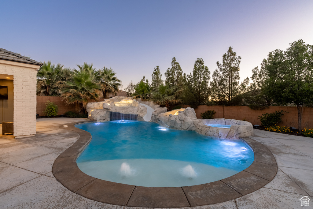 Pool at dusk with a fenced backyard, a patio, and a pool with connected hot tub
