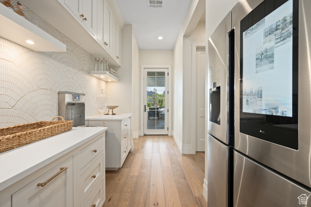 Kitchen featuring stainless steel fridge with ice dispenser, light wood-type flooring, light countertops, white cabinetry, and recessed lighting