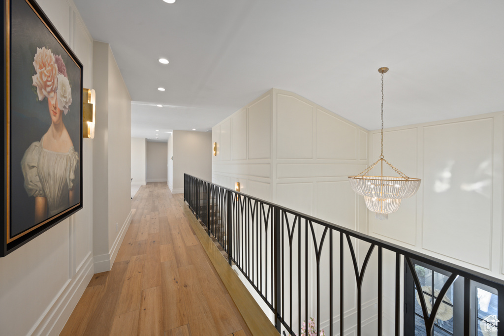 Hallway with a chandelier, a decorative wall, light wood finished floors, recessed lighting, and an upstairs landing
