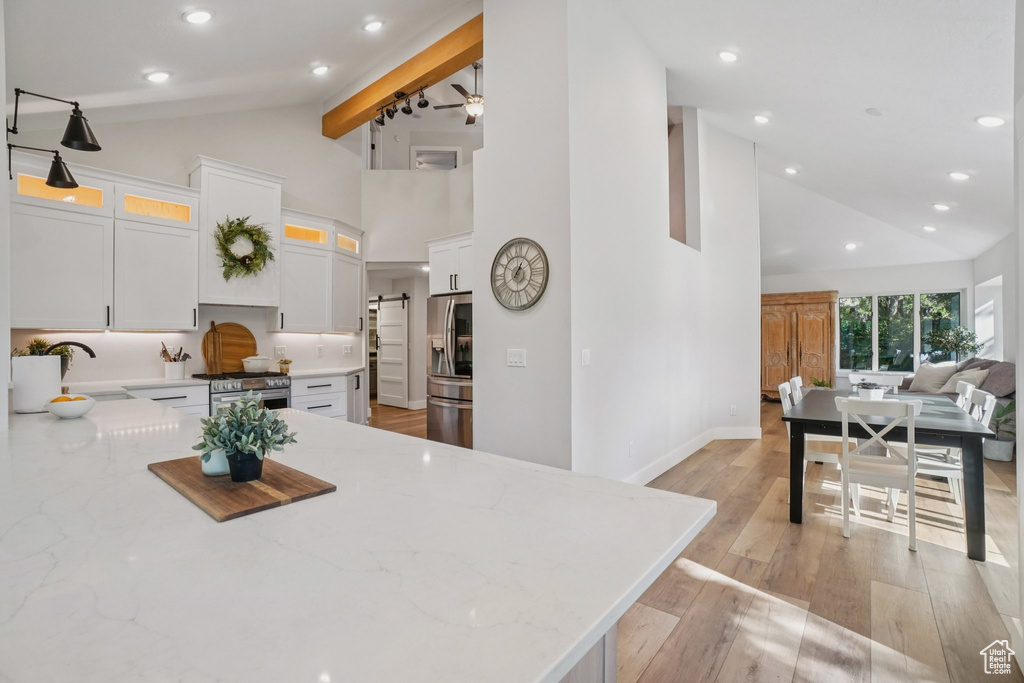 Kitchen with high vaulted ceiling, light stone countertops, stainless steel appliances, white cabinets, and open floor plan