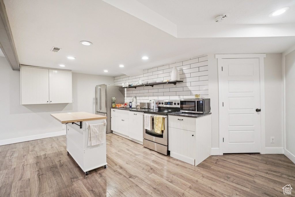 Kitchen featuring appliances with stainless steel finishes, tasteful backsplash, light wood-style flooring, white cabinetry, and recessed lighting
