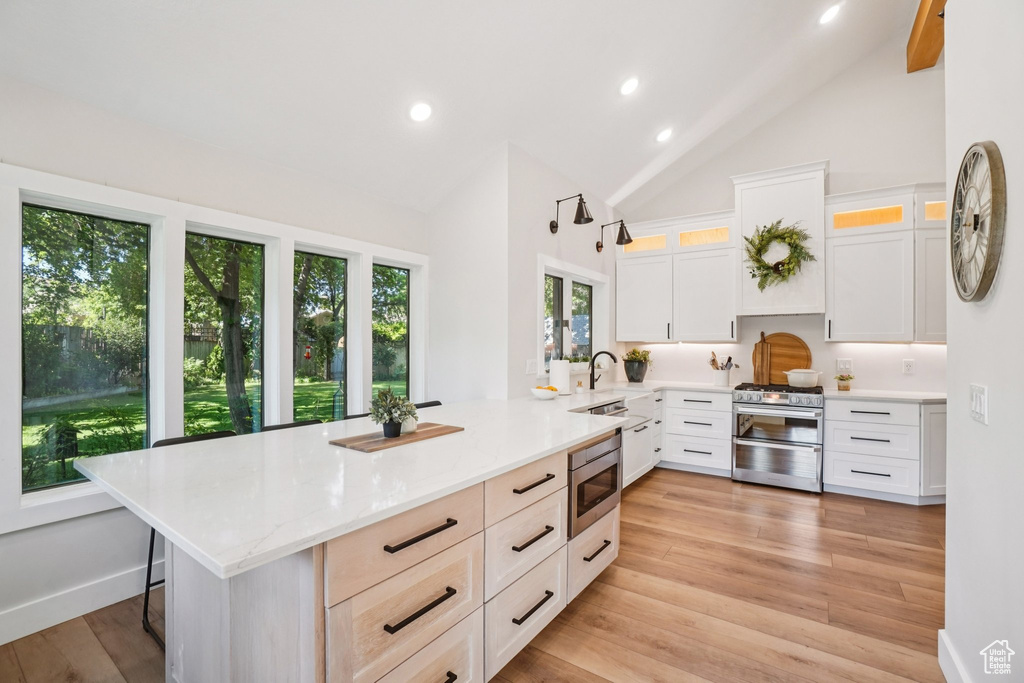 Kitchen featuring high vaulted ceiling, appliances with stainless steel finishes, a peninsula, recessed lighting, and glass insert cabinets