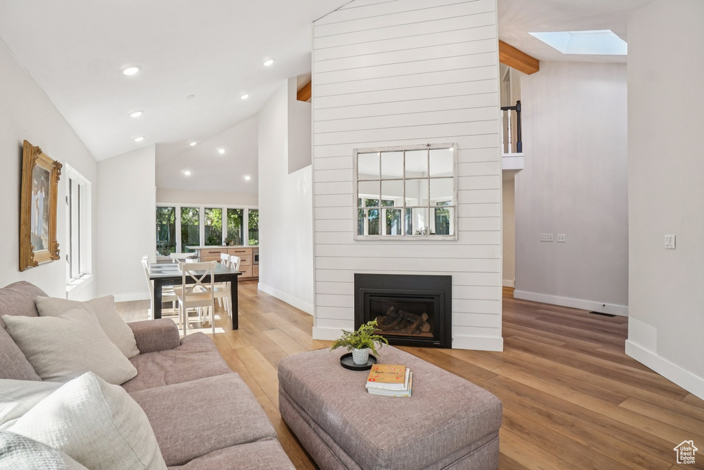 Living area with a skylight, wood finished floors, lofted ceiling, a fireplace, and recessed lighting