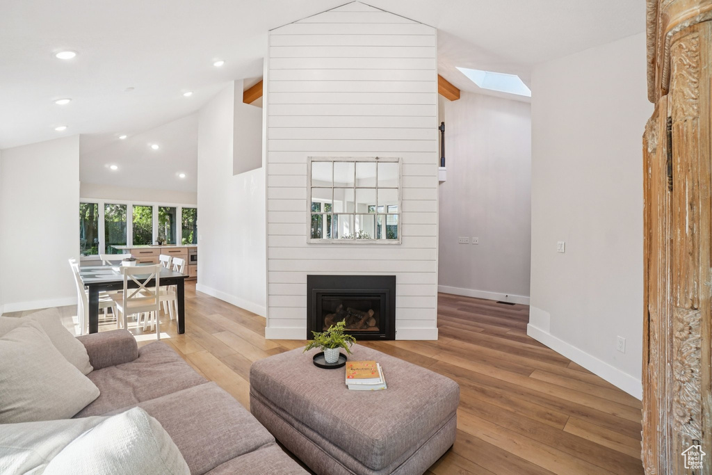 Living room with vaulted ceiling, light wood finished floors, a skylight, a fireplace, and recessed lighting