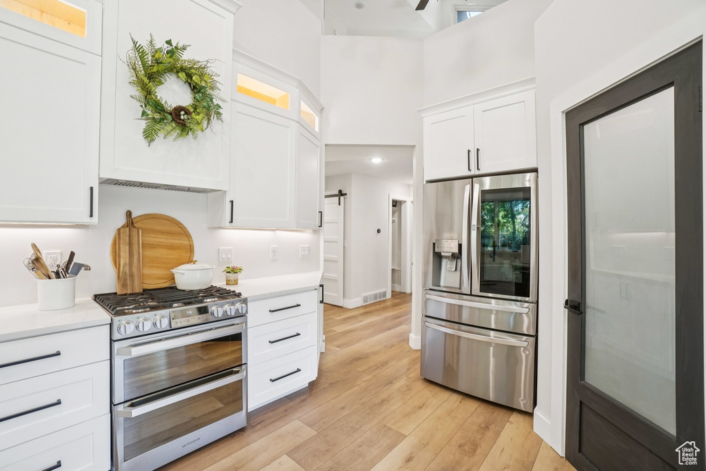Kitchen featuring stainless steel appliances, light countertops, white cabinetry, and a towering ceiling