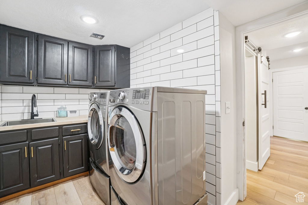 Laundry room featuring independent washer and dryer, cabinet space, light wood-type flooring, a barn door, and recessed lighting