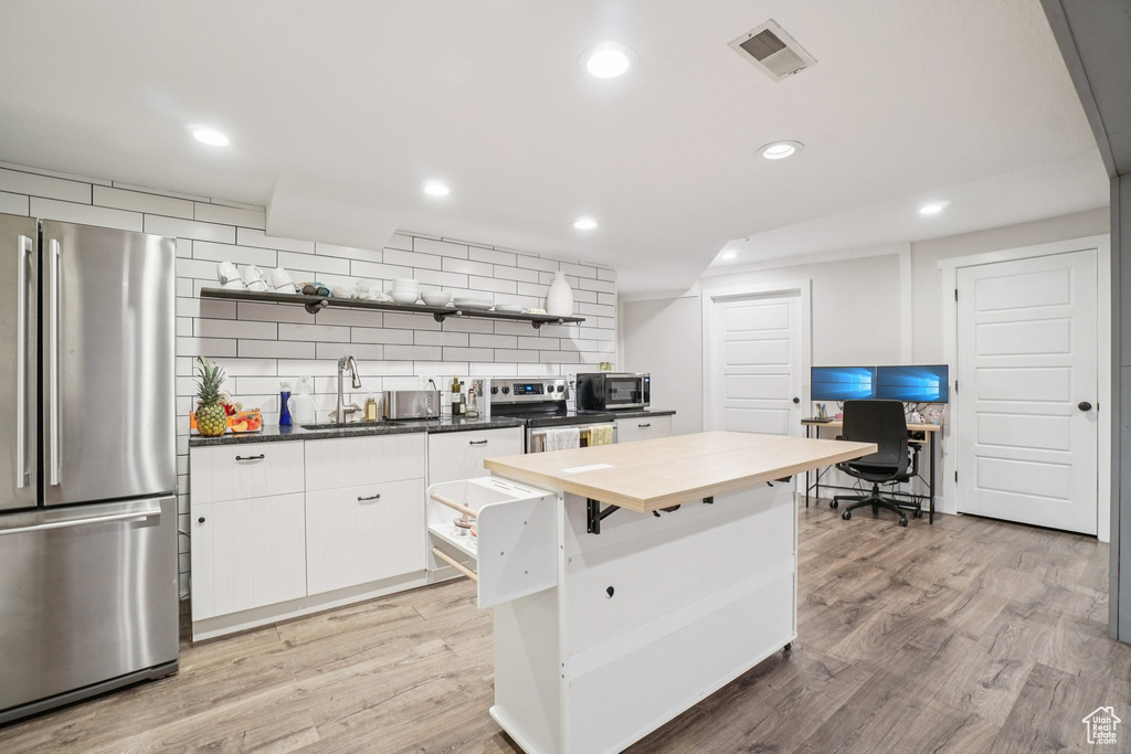 Kitchen with open shelves, stainless steel appliances, decorative backsplash, light wood-style flooring, and butcher block countertops