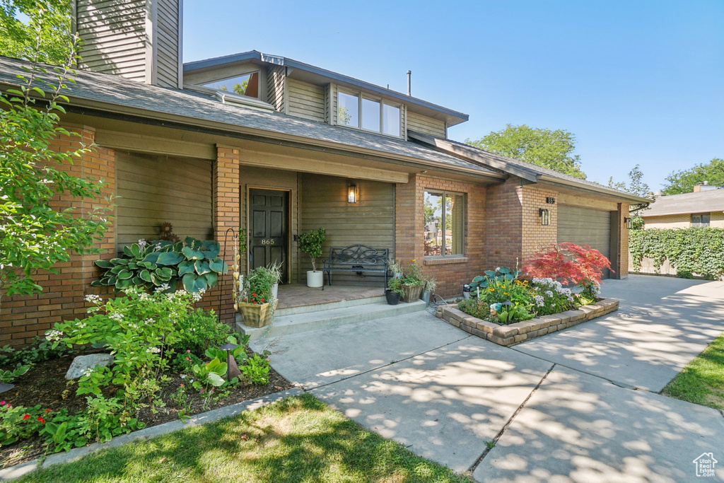 View of front of property with an attached garage, brick siding, a porch, and concrete driveway