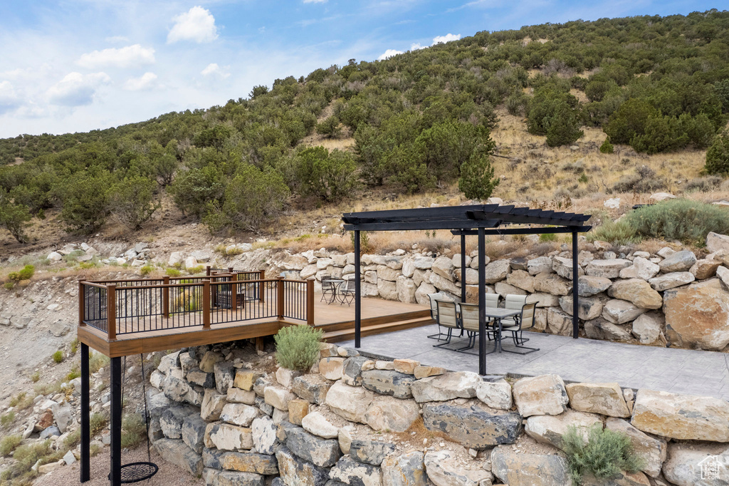 View of patio / terrace with a deck, outdoor dining area, a view of trees, and a pergola