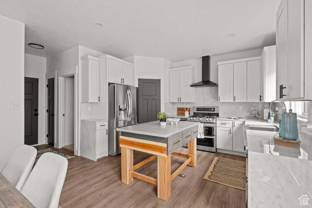 Kitchen featuring wall chimney range hood, appliances with stainless steel finishes, white cabinetry, and tasteful backsplash