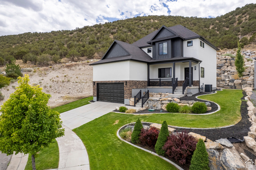 View of front of property with concrete driveway, stone siding, a front lawn, and a porch