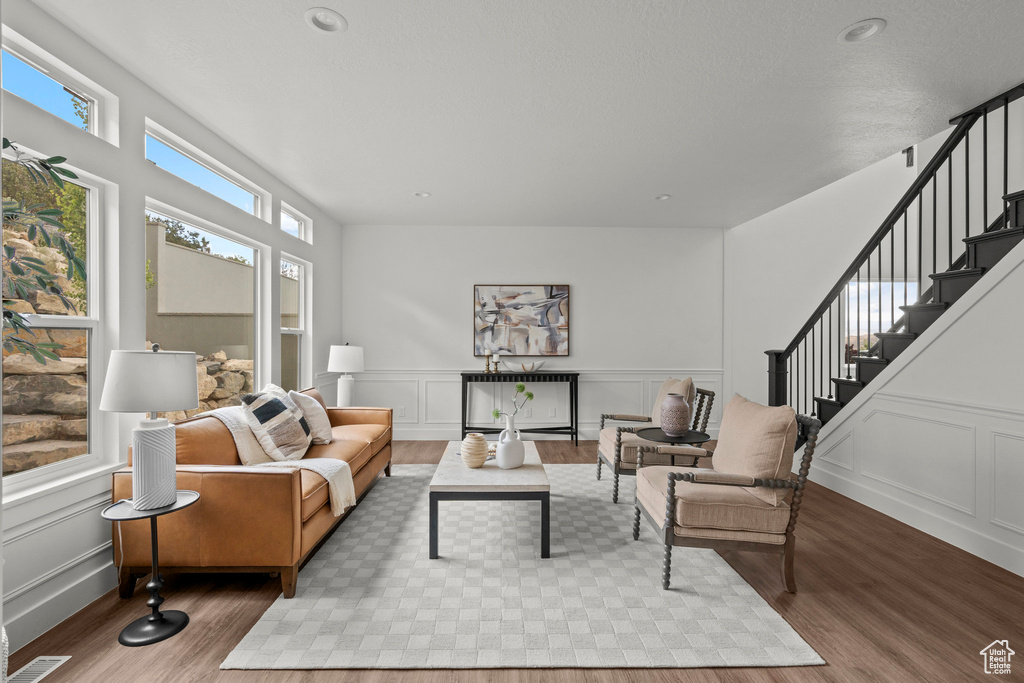 Living room featuring wood finished floors, a decorative wall, stairs, and a wainscoted wall