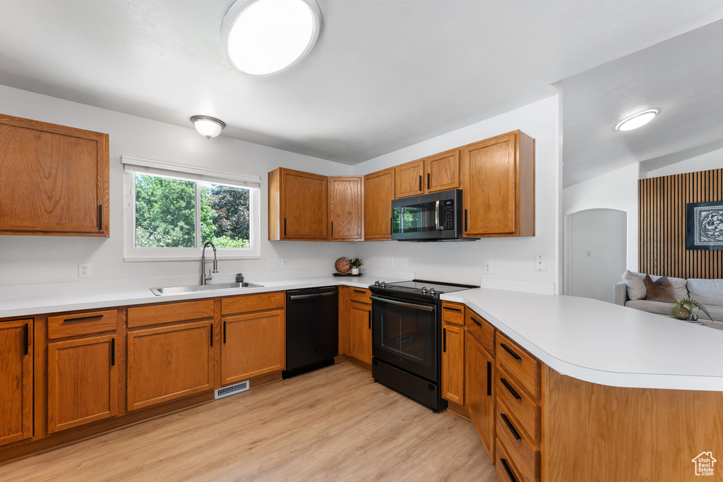 Kitchen featuring black appliances, a peninsula, light countertops, and light wood-style floors