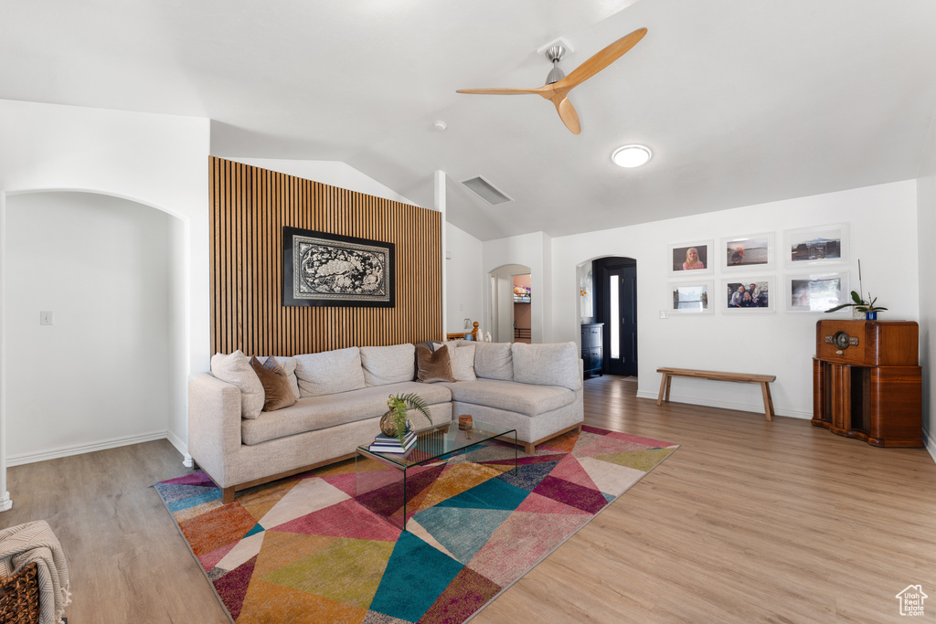 Living room with arched walkways, lofted ceiling, a ceiling fan, and light wood-type flooring
