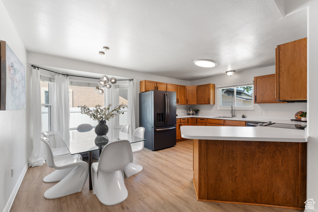 Kitchen with fridge with ice dispenser, brown cabinetry, light countertops, light wood-style floors, and a peninsula
