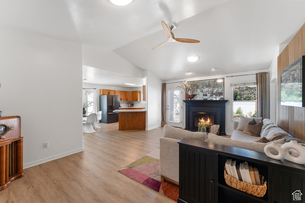Living room with lofted ceiling, a tiled fireplace, light wood-style flooring, and ceiling fan