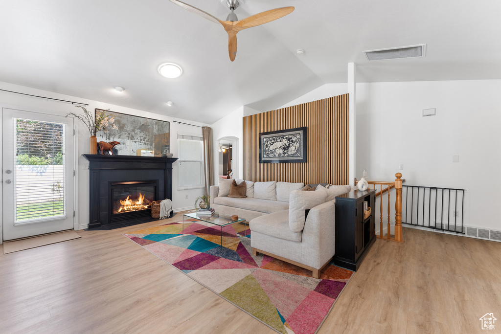 Living area featuring lofted ceiling, arched walkways, wood finished floors, a ceiling fan, and a fireplace with flush hearth