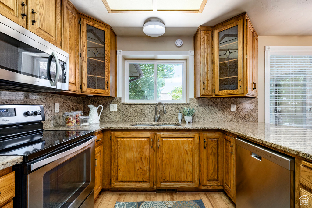 Kitchen featuring appliances with stainless steel finishes, brown cabinets, light wood-type flooring, and light stone counters