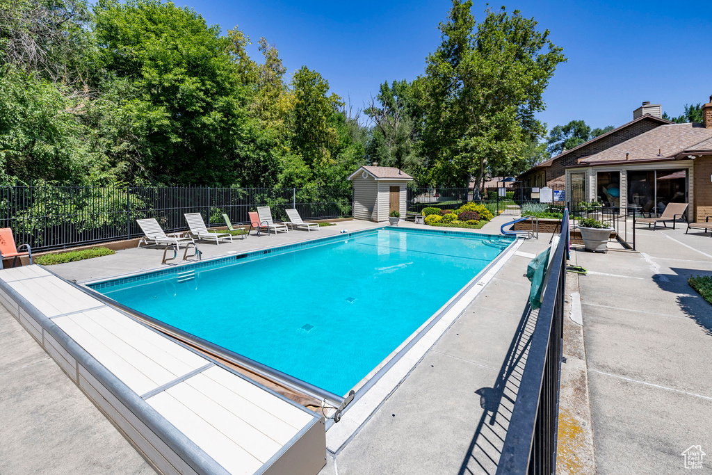 Community pool with a patio area, a storage unit, and view of wooded area