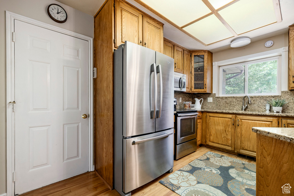 Kitchen with stainless steel appliances, brown cabinetry, light stone counters, and decorative backsplash