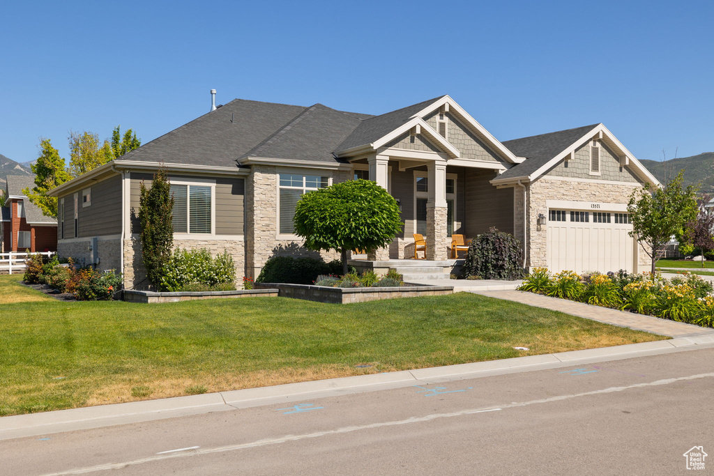 Craftsman house with stone siding, a front lawn, and a garage