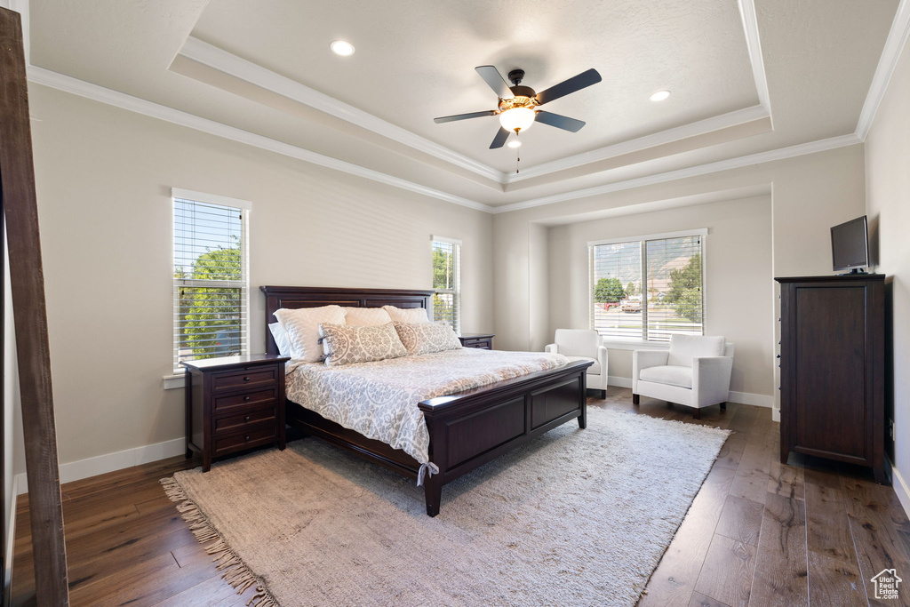 Bedroom featuring a raised ceiling, multiple windows, hardwood / wood-style floors, crown molding, and recessed lighting