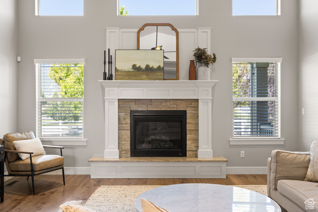 Living area with wood finished floors, a high ceiling, a glass covered fireplace, and healthy amount of natural light