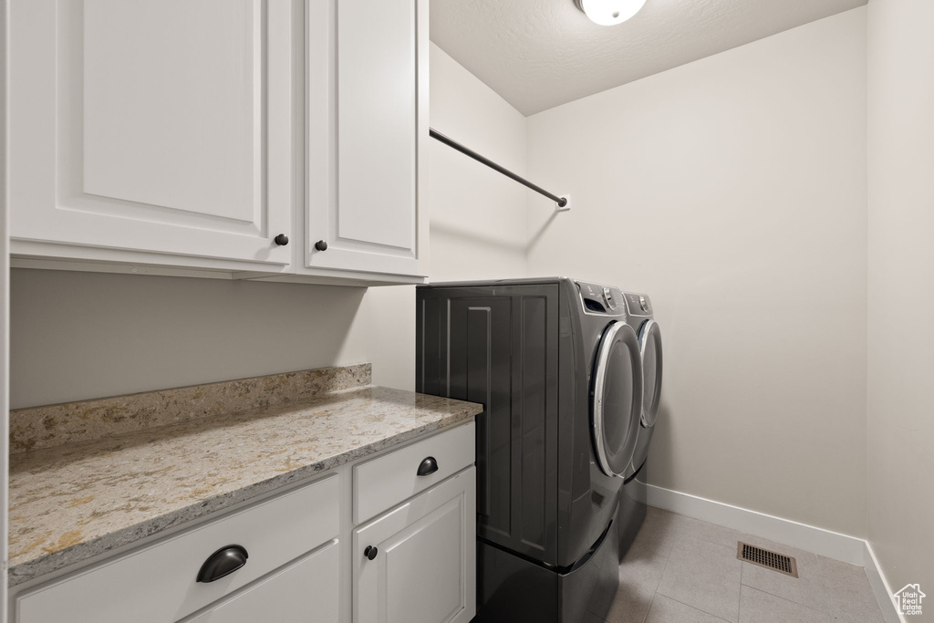 Laundry area featuring washer and clothes dryer, cabinet space, and tile patterned floors