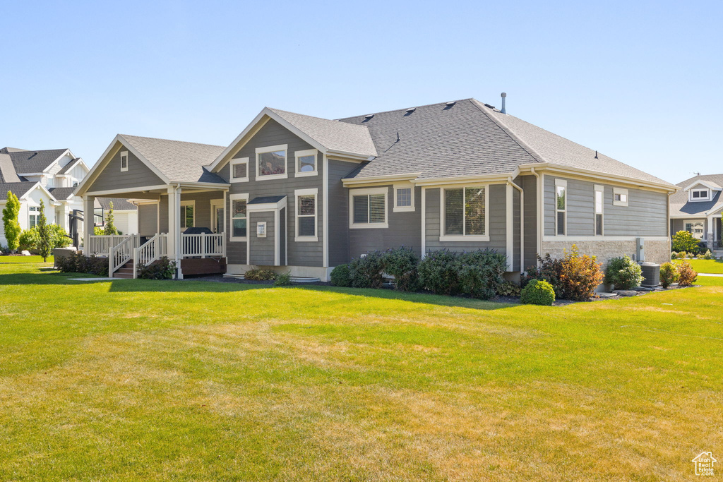 Back of house with covered porch, a lawn, and a shingled roof