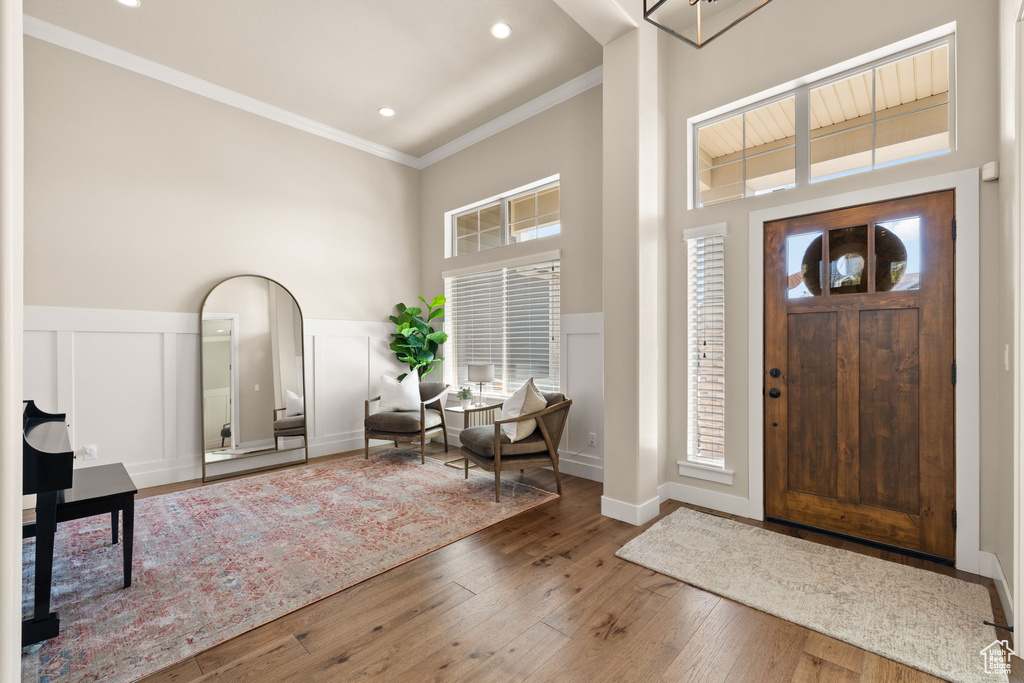 Foyer entrance featuring a towering ceiling, crown molding, hardwood / wood-style floors, healthy amount of natural light, and a wainscoted wall