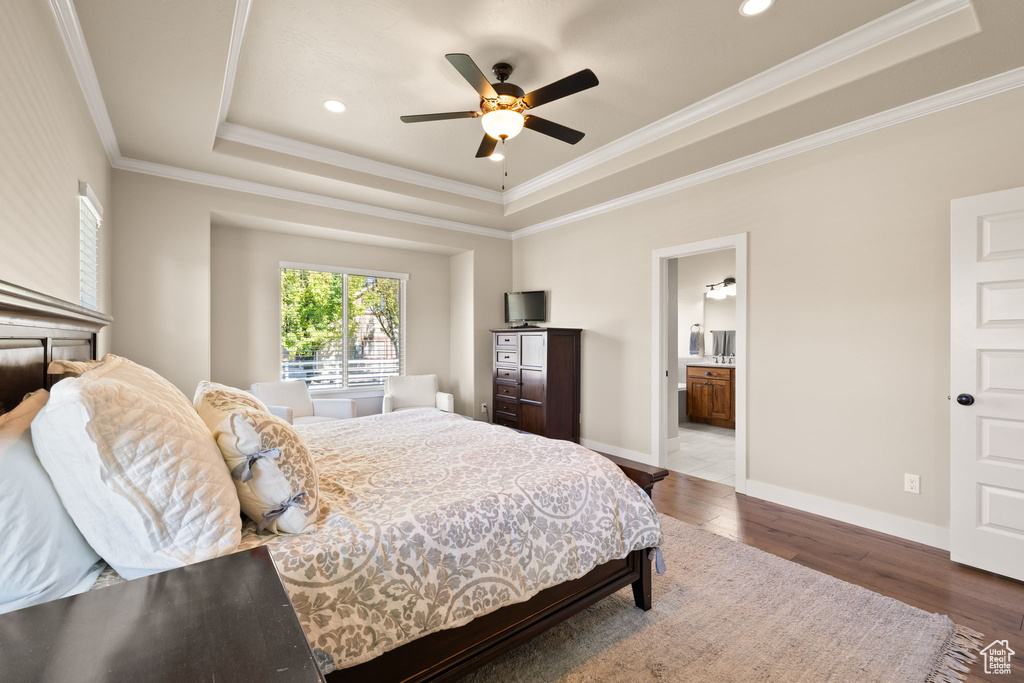 Bedroom with a raised ceiling, wood finished floors, crown molding, recessed lighting, and ensuite bath