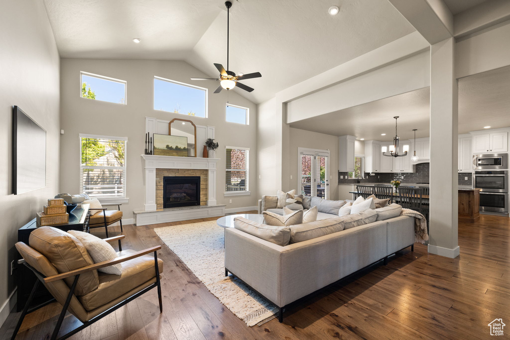 Living room with a tiled fireplace, dark wood-type flooring, ceiling fan, high vaulted ceiling, and a chandelier