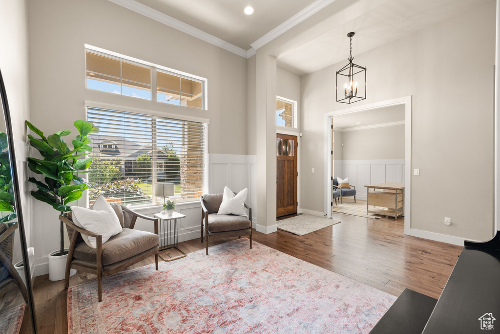 Living area featuring crown molding, a chandelier, wood finished floors, a wainscoted wall, and a towering ceiling