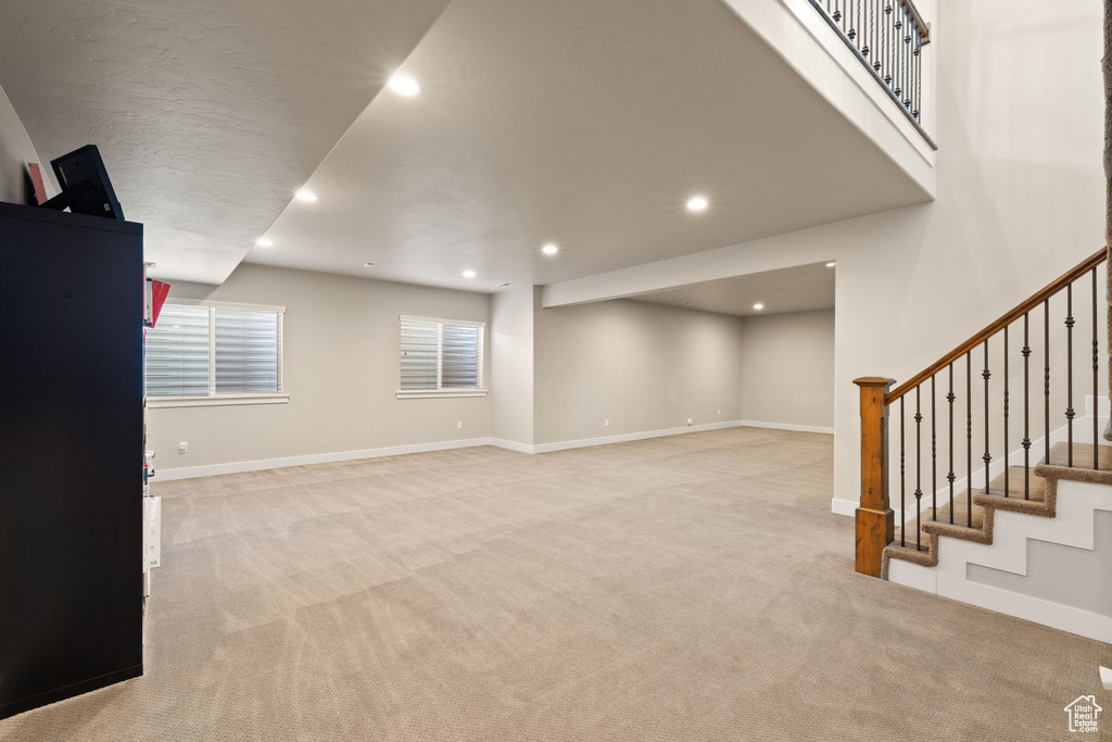 Unfurnished living room featuring light colored carpet, stairway, and recessed lighting