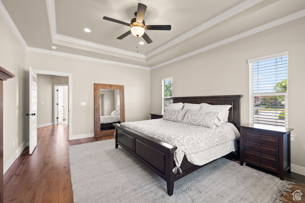 Bedroom with a raised ceiling, multiple windows, wood-type flooring, ornamental molding, and recessed lighting