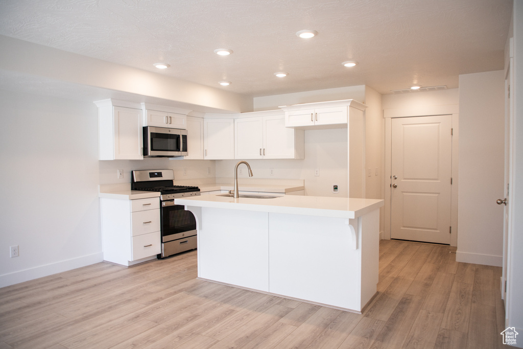 Kitchen with appliances with stainless steel finishes, light wood-style floors, a kitchen island with sink, white cabinets, and light countertops