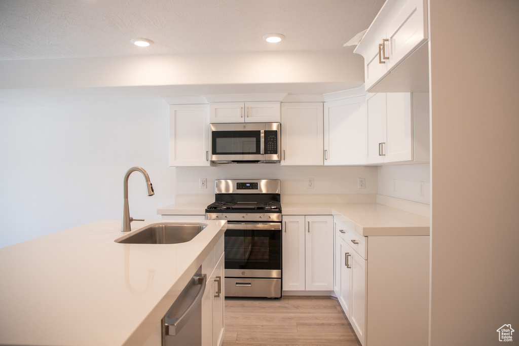Kitchen with stainless steel appliances, light countertops, light wood-style floors, white cabinetry, and recessed lighting