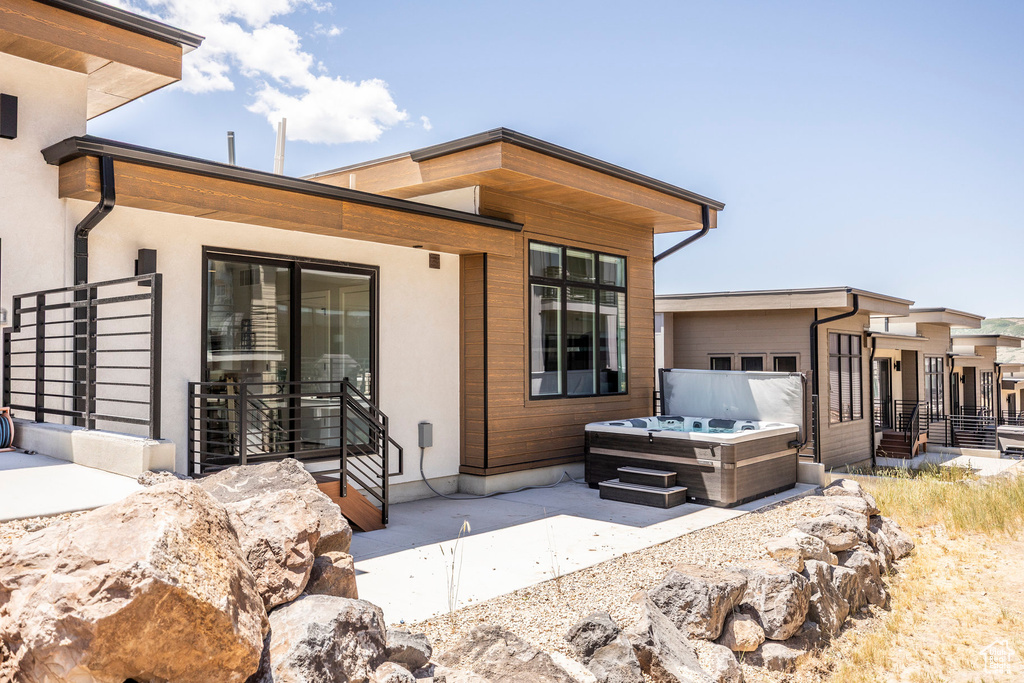 Rear view of property featuring a hot tub, a patio, and stucco siding