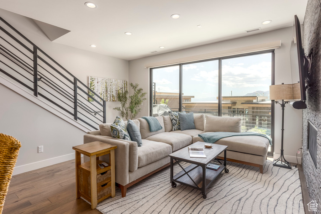 Living room with plenty of natural light, light wood finished floors, recessed lighting, stairs, and a glass covered fireplace